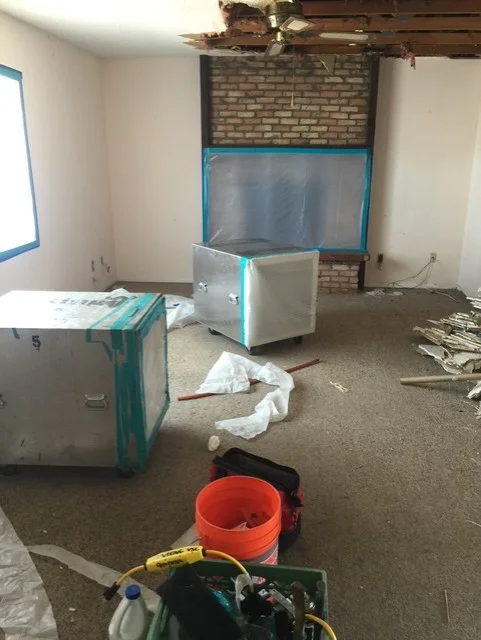 Interior demolition in progress with exposed brick fireplace, drywall removal, and construction equipment