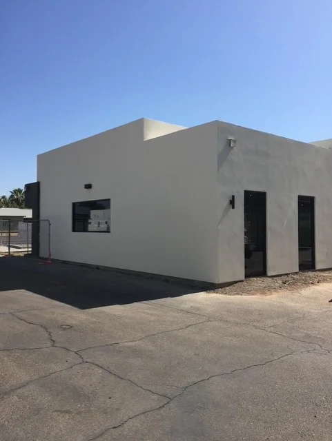 Modern commercial building with gray stucco exterior, flat roof, and black-framed windows and doors