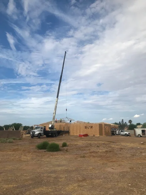 Wood-framed house structure with crane lifting materials during construction phase
