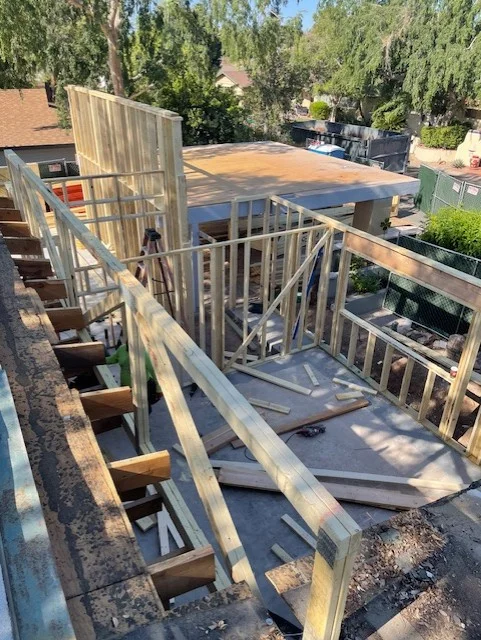 Wood framing for second-story addition with floor joists, wall studs, and railings under construction