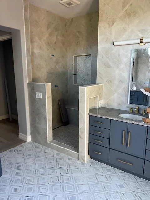 Master bathroom with marble shower surround, navy vanity, and patterned tile flooring