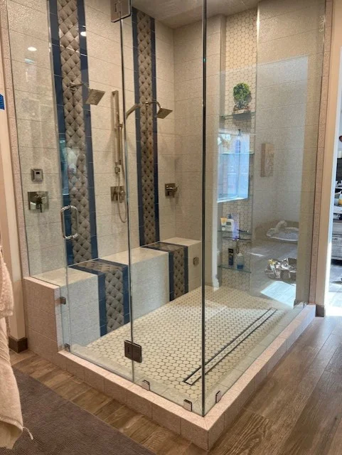 Frameless glass shower with mosaic tile accents, bench seat, and coordinating floor tile