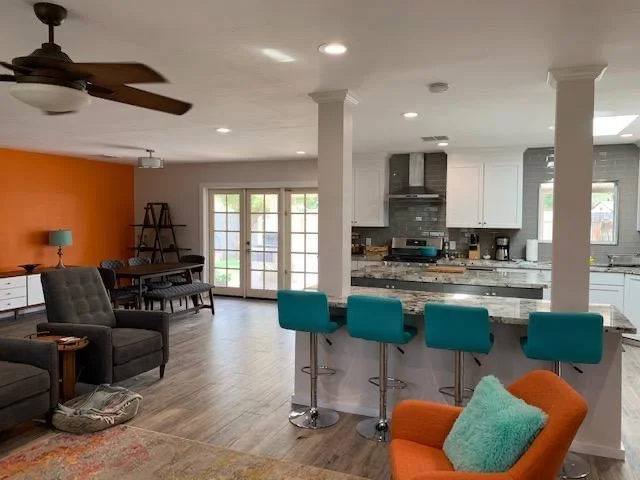 Open concept kitchen with white cabinets, granite counters, island seating, and adjacent living room with accent walls