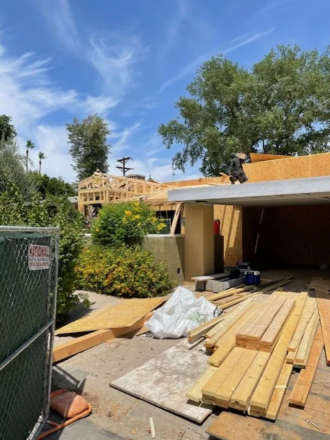 Wood framing and roof structure under construction with lumber staging and concrete foundation