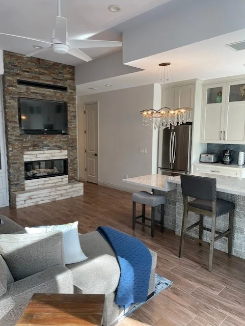 Open concept living room with stone fireplace, hardwood floors, and modern kitchen with white cabinets