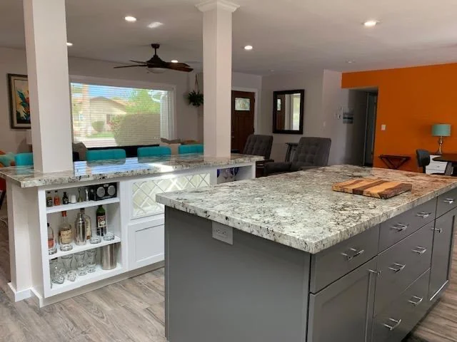 Modern kitchen with granite counters, white cabinetry, gray island, and open living area