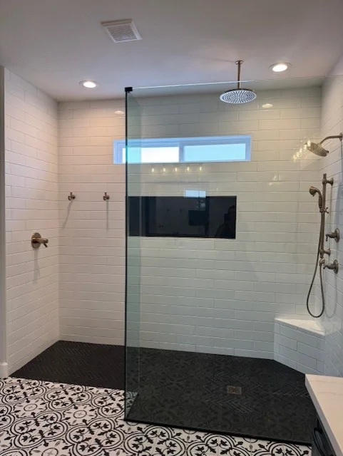 Modern bathroom with white subway tile shower, frameless glass door, black patterned floor tile, and rainfall showerhead