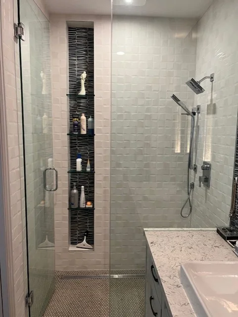 Frameless glass shower enclosure with subway tile walls, built-in black niche shelving, and chrome fixtures
