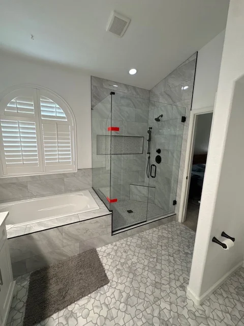 Frameless glass shower with marble tile, white soaking tub, and geometric floor tile in renovated bathroom