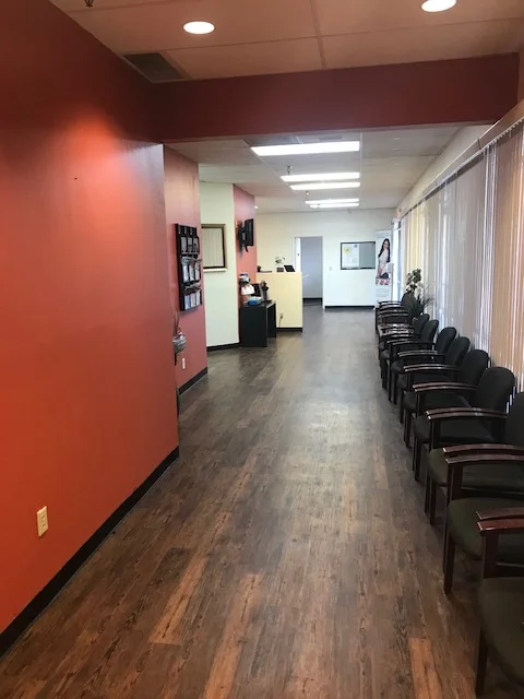 Dental office hallway with rust-red wall, wood-look vinyl flooring, recessed lights, and waiting area seating