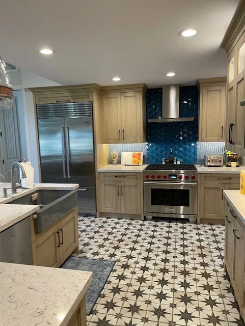 Kitchen with light wood cabinets, blue tile backsplash, stainless steel appliances, and geometric floor tile